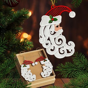 May include: Embroidered Santa Claus Christmas ornament and earrings set. The ornament and earrings feature a red and white Santa hat, white beard, and a sprig of holly. The earrings are displayed in a small box. The image has the text "2 sizes".