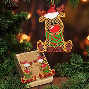 Puede incluir: Adorno y pendientes navideños con diseño de reno. El reno tiene un gorro rojo y una bufanda verde y roja. Los pendientes están en una caja. También se ve el texto "2 tamaños".