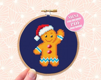 May include: A mini cross stitch pattern PDF for a gingerbread man wearing a Santa hat. The pattern is displayed on a blue background in a wooden embroidery hoop.