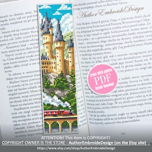 May include: A cross-stitch bookmark featuring a castle design with a train, set against a blue sky with clouds. The bookmark is placed in an open book. Text on the bookmark reads "Author Embroide Design".