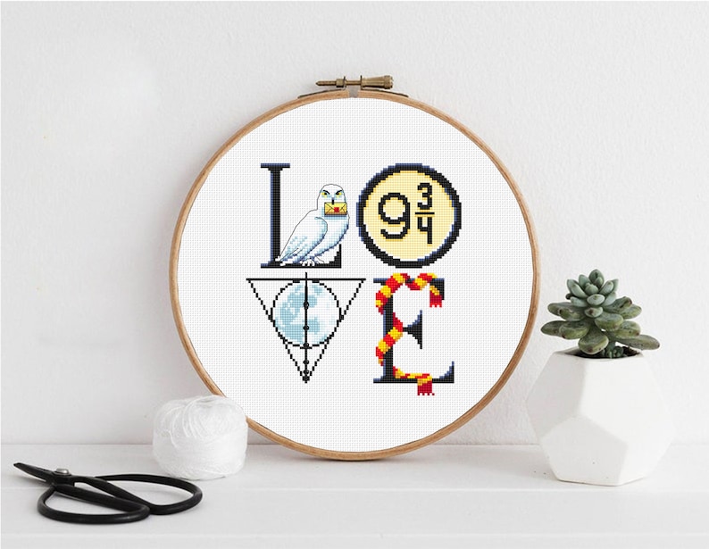 May include: Cross stitch pattern of the word "LOVE" with Harry Potter themed icons. The "L" is a white owl holding a letter, the "O" is the platform 9 3/4 sign, the "V" is the Deathly Hallows symbol, and the "E" is a red and gold scarf.