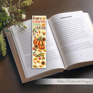 May include: A bookmark with the text "Happy Pumpkin Spice Season" and autumn-themed illustrations of pumpkins, sunflowers, and leaves. The bookmark is placed in an open book next to a small pumpkin and a vase of flowers.