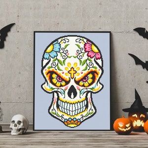Puede incluir: Una impresi&oacute;n enmarcada de una calavera de az&uacute;car colorida con dise&ntilde;os florales y una cruz en la frente. La calavera es blanca con acentos amarillos, rojos, azules y verdes. El fondo es azul claro.