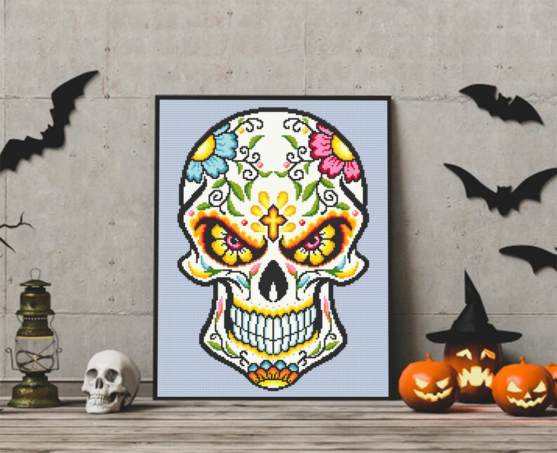 Puede incluir: Una impresi&oacute;n enmarcada de una calavera de az&uacute;car colorida con dise&ntilde;os florales y una cruz en la frente. La calavera es blanca con acentos amarillos, rojos, azules y verdes. El fondo es azul claro.