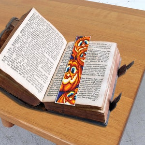 May include: A vintage book with a colorful pumpkin bookmark. The bookmark is made of beads and features a smiling pumpkin face.