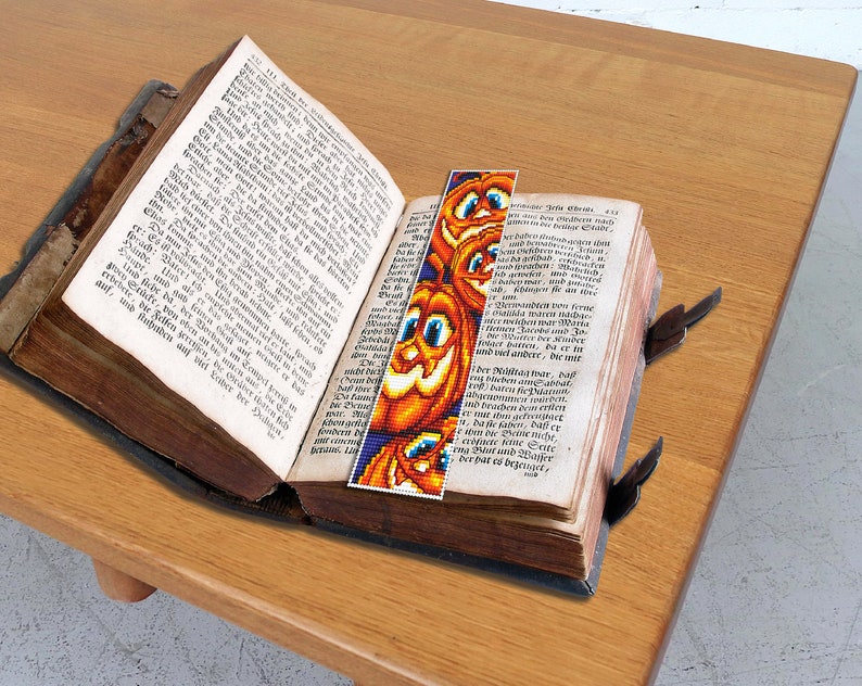 May include: A vintage book with a colorful pumpkin bookmark. The bookmark is made of beads and features a smiling pumpkin face.
