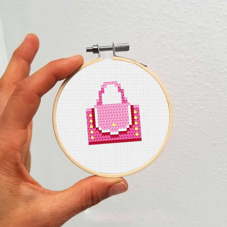 May include: A pink and yellow cross-stitch design of a handbag in a wooden embroidery hoop.