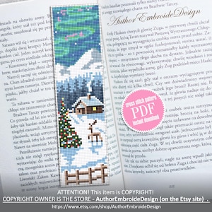 May include: Cross-stitch bookmark featuring a winter landscape with a cabin, evergreen tree, and deer under a starry sky. The bookmark is a cross-stitch pattern with a snowy scene and a wooden fence.