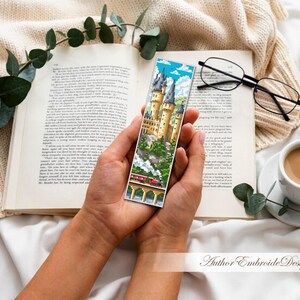 Puede incluir: Un marcap&aacute;ginas colorido con un castillo y un tren sobre un puente. Se sostiene sobre un libro abierto, con una taza de caf&eacute;, gafas y una vela. Un art&iacute;culo decorativo para los amantes de la lectura.