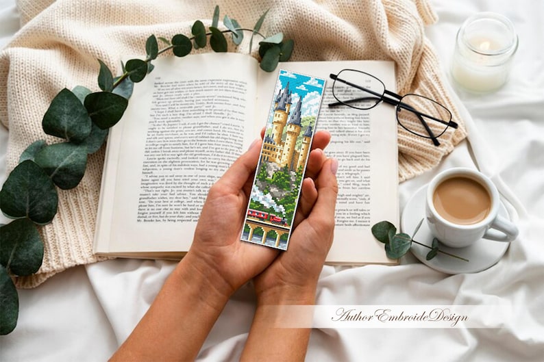 Puede incluir: Un marcap&aacute;ginas colorido con un castillo y un tren sobre un puente. Se sostiene sobre un libro abierto, con una taza de caf&eacute;, gafas y una vela. Un art&iacute;culo decorativo para los amantes de la lectura.