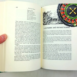 Op de afbeelding: Een open boek met een zwart-witte illustratie van een bos sc&egrave;ne op de linkerpagina en een zwart en groen roulettewiel op de rechterpagina. De tekst op de linkerpagina luidt "The Two Towers" en "Bigger of all, Huge, old and tall, If ever you meet me You would never forget me. You were old when I was young, But you weren't as strong. You couldn't catch me, And I never met..."