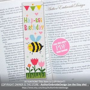 Puede incluir: Un marcapáginas de punto de cruz hecho a mano con las palabras "Hap-bee Birthday" y una abeja de dibujos animados. El marcapáginas presenta banderas, corazones y flores coloridas, colocado en un libro abierto.