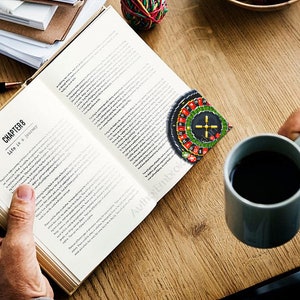 Op de afbeelding: Een persoon leest een boek met de titel "Hoofdstuk 8 Het leven is een reis". Een roulettewiel bladwijzer zit in het boek. De persoon houdt een kop koffie vast.