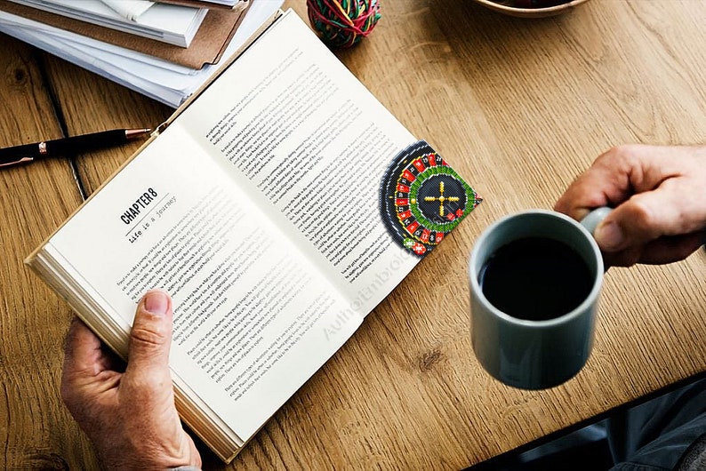 Op de afbeelding: Een persoon leest een boek met de titel "Hoofdstuk 8 Het leven is een reis". Een roulettewiel bladwijzer zit in het boek. De persoon houdt een kop koffie vast.