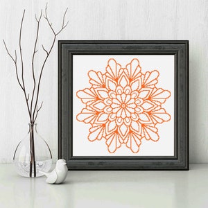 May include: A framed cross-stitch pattern of an orange mandala design. The mandala is a circular design with intricate details and a floral motif.