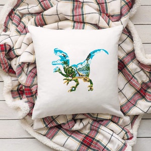 May include: White pillow with a blue dinosaur silhouette embroidered on it. The dinosaur is facing right and has a green, blue, and brown landscape inside its body.