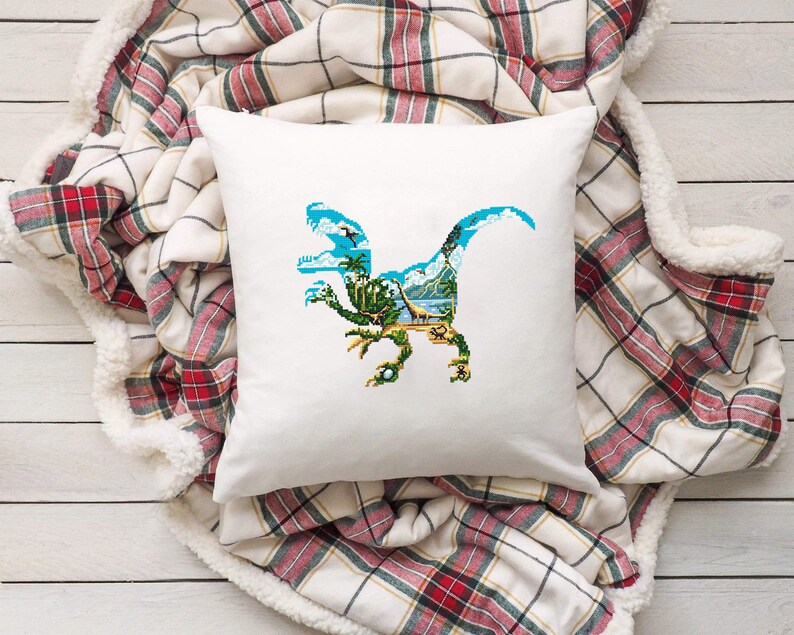 May include: White pillow with a blue dinosaur silhouette embroidered on it. The dinosaur is facing right and has a green, blue, and brown landscape inside its body.