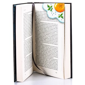 May include: A black book with a bookmark shaped like a pixelated fried egg with a green garnish. The bookmark is sticking out of the book.