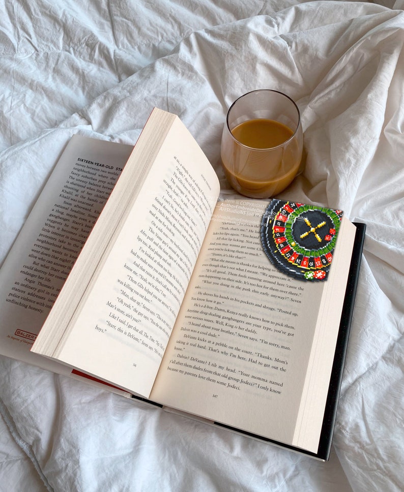 Op de afbeelding: Een close-up van een open boek met een glas koffie en een kralenroulette-bladwijzer. Het boek is open op een pagina met tekst over een tienermeisje en haar vrienden. De roulette-bladwijzer is rood, zwart en groen met witte nummers.