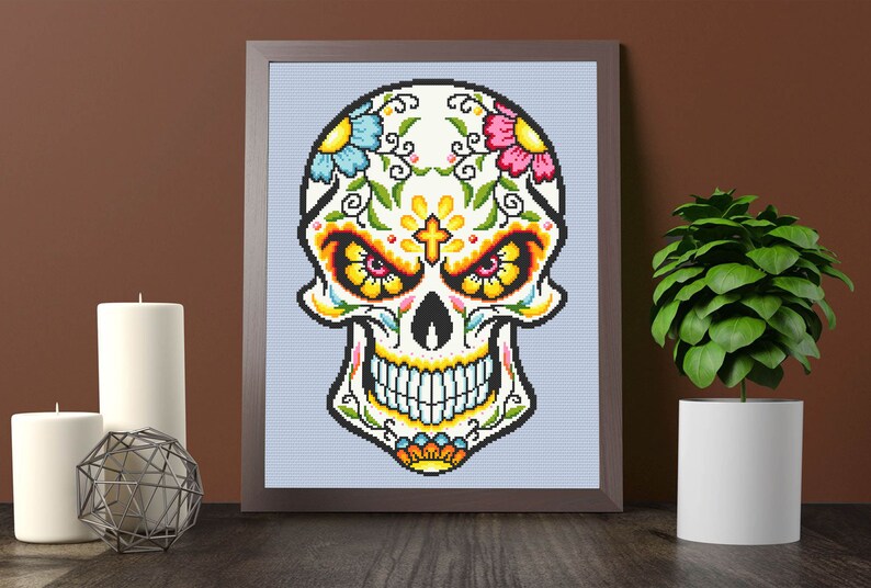 Puede incluir: Una impresi&oacute;n enmarcada de una calavera de az&uacute;car colorida con dise&ntilde;os florales y una cruz en la frente. La calavera es blanca con contornos negros y presenta flores amarillas, rosas, azules y verdes.