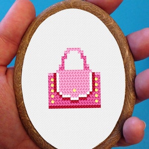 May include: A pink and yellow cross-stitch design of a handbag in a wooden embroidery hoop.