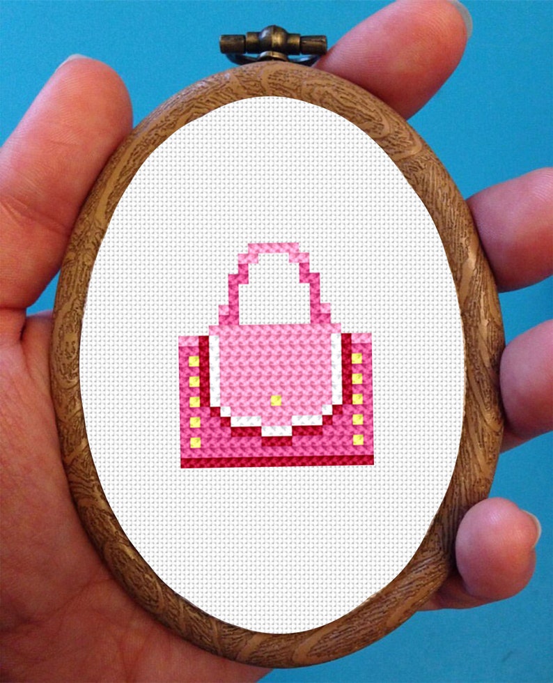 May include: A pink and yellow cross-stitch design of a handbag in a wooden embroidery hoop.