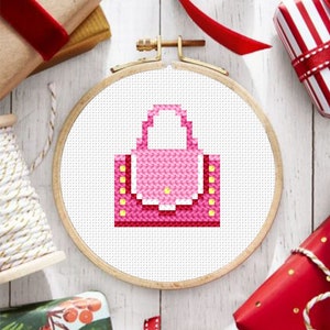 May include: A pink and yellow cross-stitch design of a handbag in a wooden embroidery hoop.