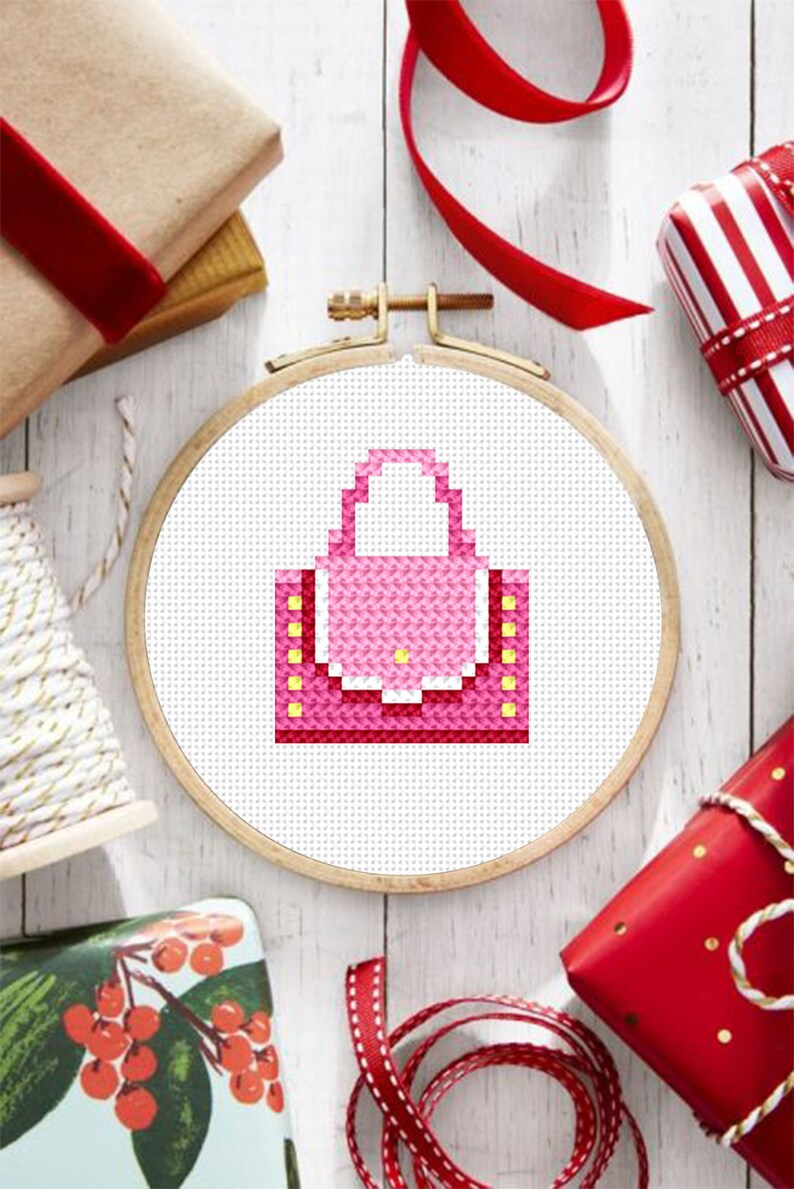 May include: A pink and yellow cross-stitch design of a handbag in a wooden embroidery hoop.