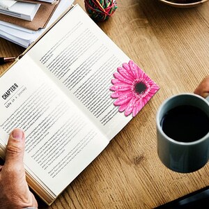 Puede incluir: Un libro abierto con el Cap&iacute;tulo 8 titulado "La vida es un viaje" est&aacute; sobre una mesa de madera. Un marcap&aacute;ginas de gerbera rosa con gotas de agua descansa en la p&aacute;gina. Una taza gris llena de l&iacute;quido oscuro est&aacute; cerca.
