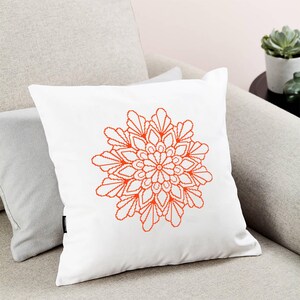 May include: White cushion with an orange mandala design. The mandala is a geometric pattern with a circular shape.