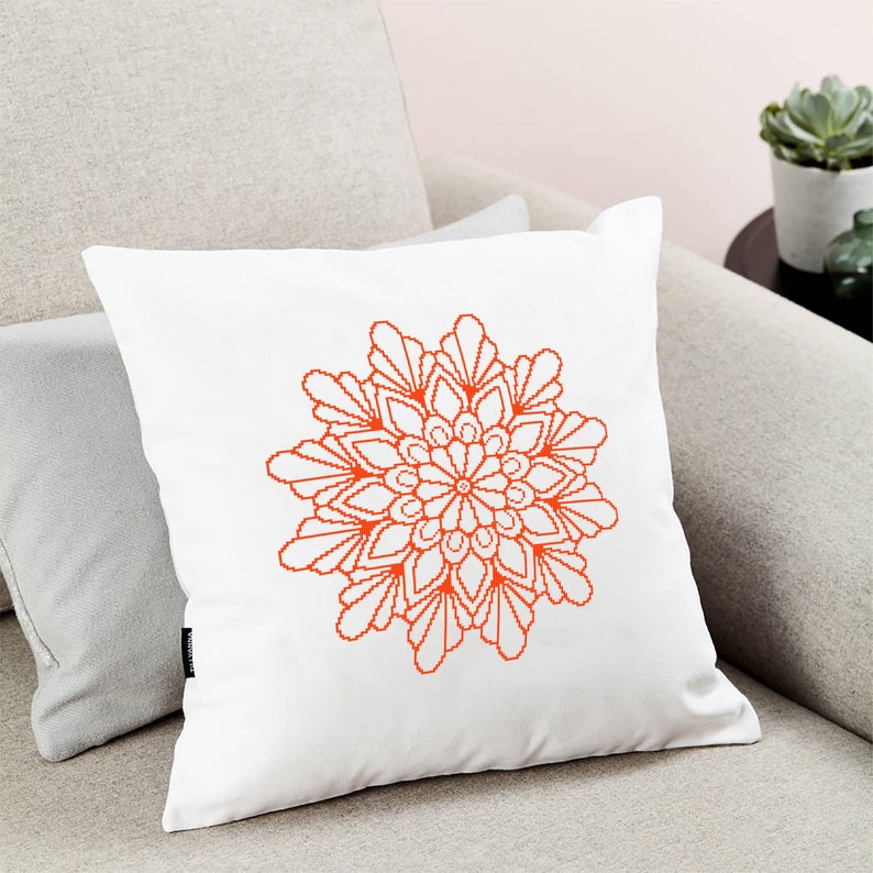 May include: White cushion with an orange mandala design. The mandala is a geometric pattern with a circular shape.