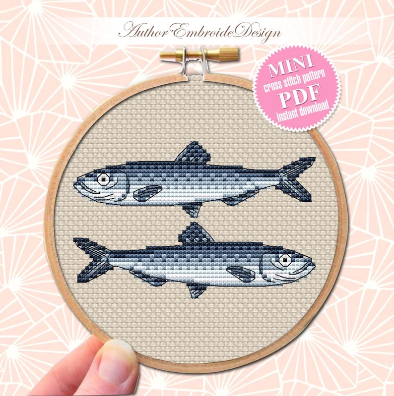 May include: A cross stitch pattern of two blue fish on a beige background. The pattern is in a wooden embroidery hoop. The text "MINI cross stitch pattern PDF instant download" is on a pink circle.