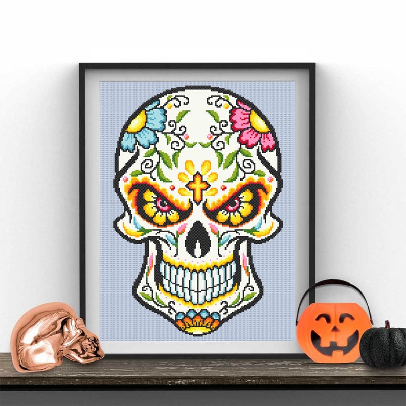 Puede incluir: Una calavera de az&uacute;car colorida con flores y dise&ntilde;os intrincados. La calavera es blanca con acentos amarillos, naranjas, rojos, azules y verdes. La calavera sonr&iacute;e con una cruz en la frente.