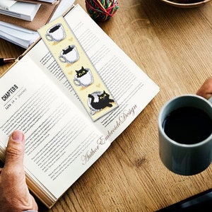 Puede incluir: Un marcap&aacute;ginas amarillo con gatos negros asom&aacute;ndose de tazas de caf&eacute;. El marcap&aacute;ginas est&aacute; marcado con "Author Embroide Design".