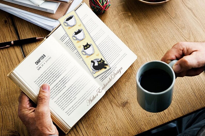 Puede incluir: Un marcap&aacute;ginas amarillo con gatos negros asom&aacute;ndose de tazas de caf&eacute;. El marcap&aacute;ginas est&aacute; marcado con "Author Embroide Design".