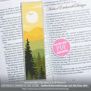 Könnte beinhalten: Kreuzstich-Lesezeichen mit Landschaftsdesign: gelbe Sonne, Berge und Nadelbäume. Das Lesezeichen steckt in einem offenen Buch. Der Text "Author Embroide Design" ist sichtbar.