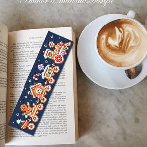 Puede incluir: Un marcap&aacute;ginas azul marino hecho a mano con un dise&ntilde;o de hombre de jengibre bordado a punto de cruz. El marcap&aacute;ginas est&aacute; colocado en un libro abierto junto a una taza de caf&eacute; con arte latte. El texto "Author Embroide Design" est&aacute; en la parte superior.