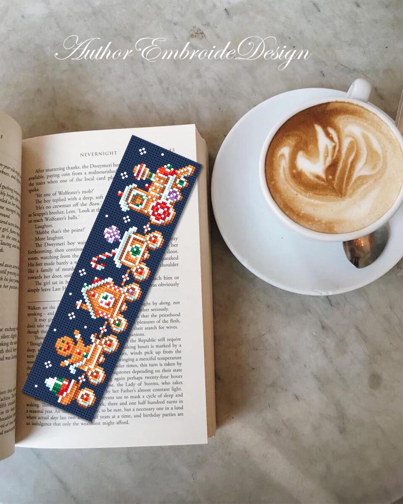 Puede incluir: Un marcap&aacute;ginas azul marino hecho a mano con un dise&ntilde;o de hombre de jengibre bordado a punto de cruz. El marcap&aacute;ginas est&aacute; colocado en un libro abierto junto a una taza de caf&eacute; con arte latte. El texto "Author Embroide Design" est&aacute; en la parte superior.