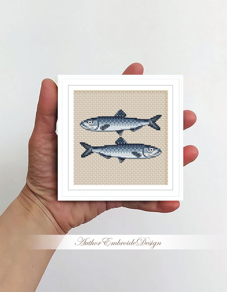 May include: A cross-stitch embroidery design featuring two blue and white fish on a beige background. The design is framed in a white frame.