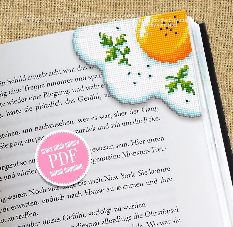 May include: A pink circle with the text "cross stitch pattern PDF instant download" in white. The circle is on a book page with text about a story. The book page is folded over and a cross stitch bookmark of a sunny-side-up egg with parsley is visible.
