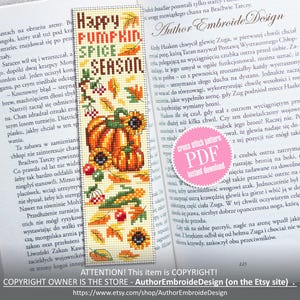 May include: Embroidered bookmark with a fall theme. The bookmark features the text "Happy Pumpkin Spice Season" with images of pumpkins, sunflowers, and autumn leaves. It is placed on an open book.