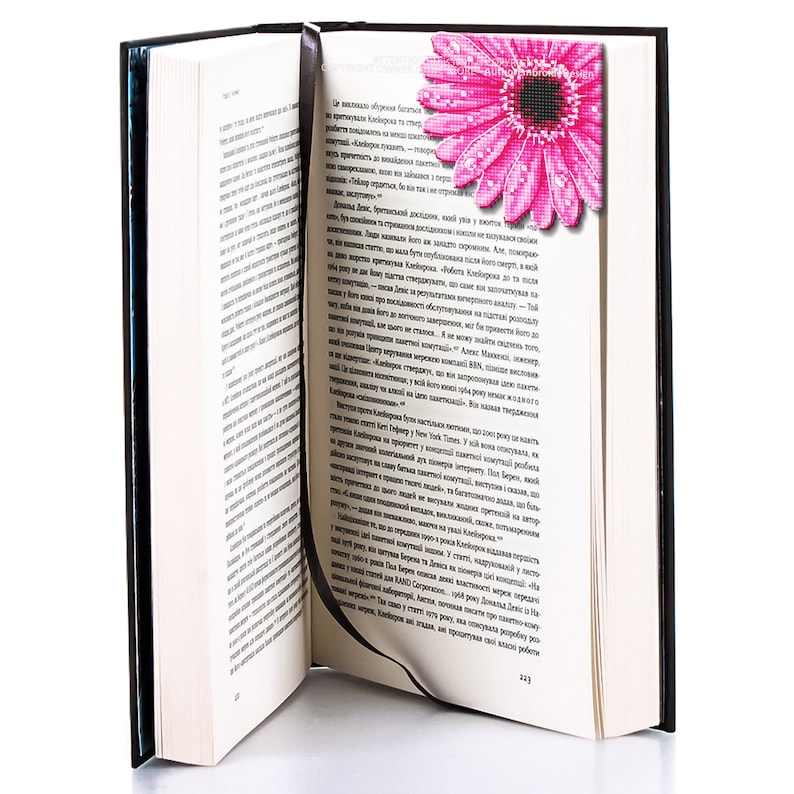 Puede incluir: Un libro abierto con cubiertas negras y p&aacute;ginas blancas, con un marcap&aacute;ginas de flores rosas con gotas de agua. El libro est&aacute; en &aacute;ngulo, revelando el texto en las p&aacute;ginas.