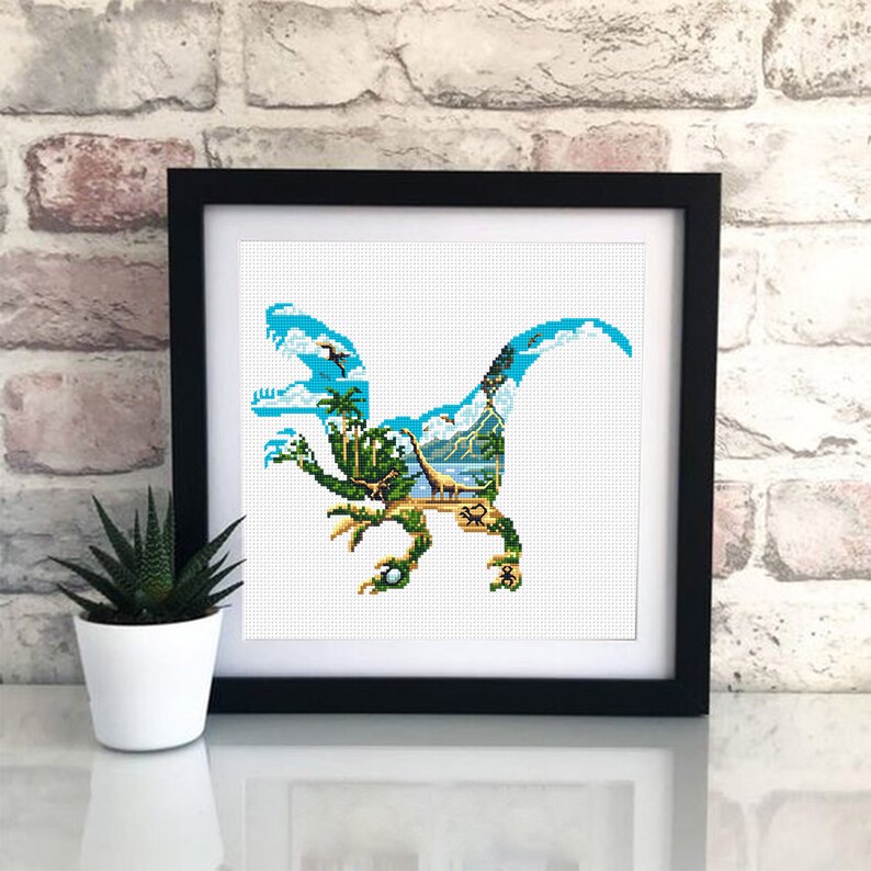 May include: A framed cross-stitch design featuring a blue dinosaur silhouette with a tropical island scene inside. The dinosaur is standing on a beach with palm trees, a volcano, and a blue sky.