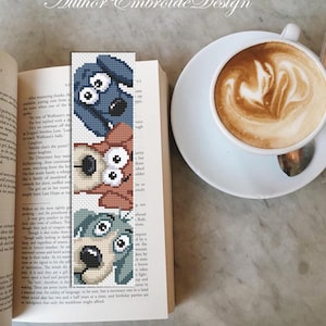 May include: An embroidered bookmark with three dog faces in blue, brown, and green, placed in an open book. A cup of coffee with latte art sits beside the book. The text "Author Embroide Design" is visible at the top of the image.