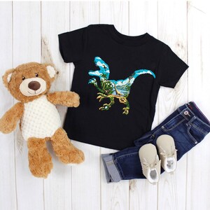 May include: Black t-shirt with a graphic print of a dinosaur silhouette with a tropical landscape inside. The dinosaur is blue and green, and the landscape is a mix of blue, green, and brown.