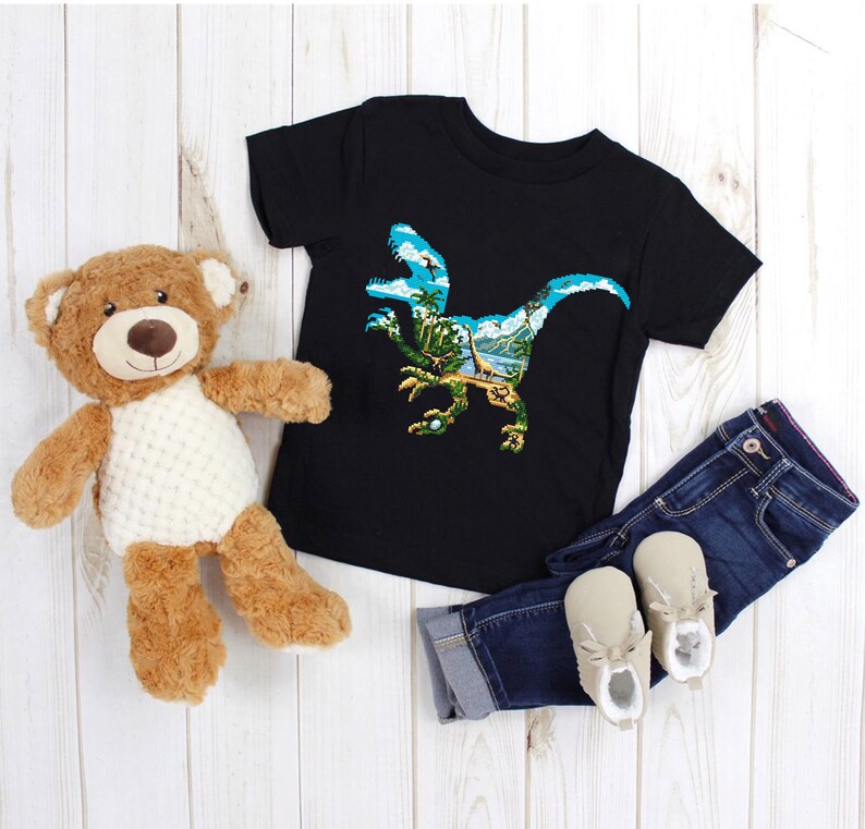 May include: Black t-shirt with a graphic print of a dinosaur silhouette with a tropical landscape inside. The dinosaur is blue and green, and the landscape is a mix of blue, green, and brown.