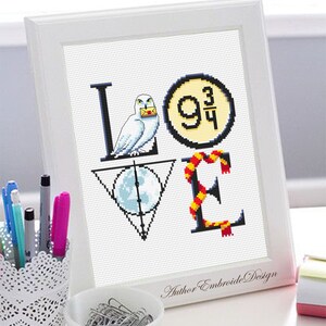 May include: A white framed cross-stitch design featuring the word "LOVE" with Harry Potter themed imagery. The "L" features a white owl holding a letter, the "O" features the platform 9 3/4 sign, the "V" features the Deathly Hallows symbol, and the "E" features a red and gold scarf.