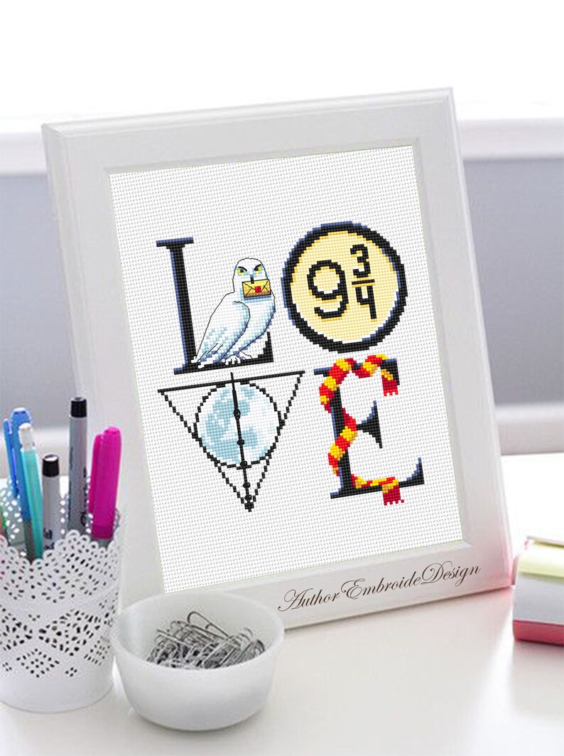 May include: A white framed cross-stitch design featuring the word "LOVE" with Harry Potter themed imagery. The "L" features a white owl holding a letter, the "O" features the platform 9 3/4 sign, the "V" features the Deathly Hallows symbol, and the "E" features a red and gold scarf.
