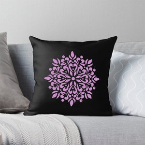 May include: A black throw pillow featuring a symmetrical, floral-like design in light purple. The design is pixelated, giving it a cross-stitch or digital art appearance. The pillow is square and appears to be made of soft fabric.