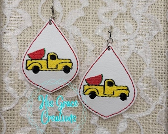 Pode incluir: Brincos brancos em forma de gota com um caminhão amarelo carregando uma fatia de melancia. Os brincos têm uma borda costurada em vermelho e ganchos prateados. O texto "His Grace Creations" está na imagem.